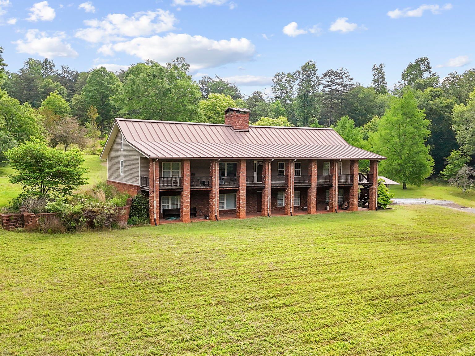 Side angle view of the main residence in soft afternoon light, brick column porch and red metal roof set against deep blue sky and dense Georgia treeline