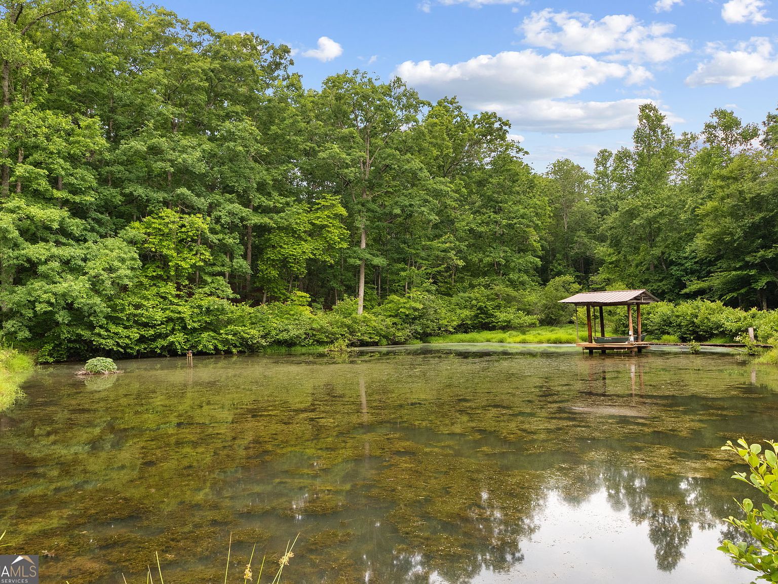 Quiet pond on the property with a small wooden gazebo on the far bank, forest reflecting on still water, summer foliage on every side