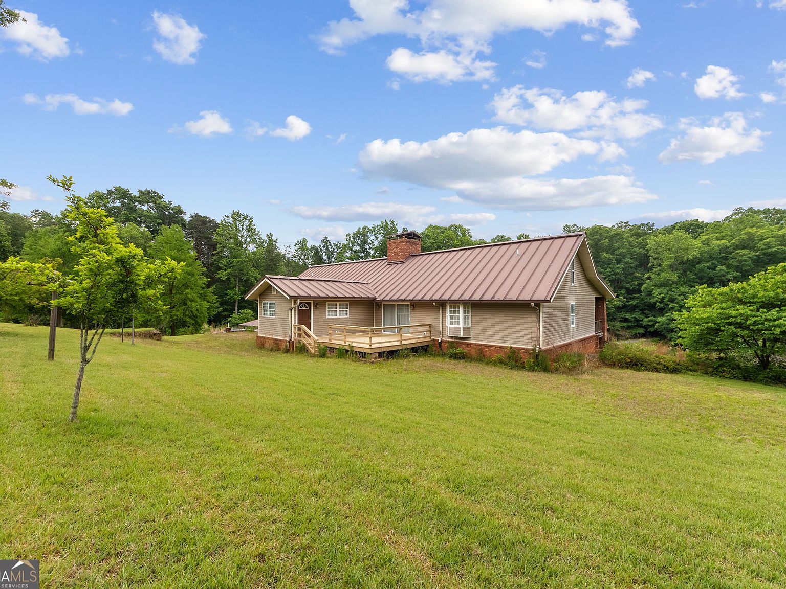 Smaller ranch-style home on the front tract with metal roof and a wide green lawn under broken cloud, surrounded by mature Georgia hardwoods