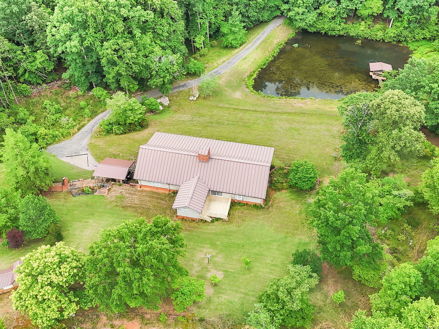Aerial view of the 4454 Ledan Ext estate showing the main residence with red metal roof tucked into woodland and a small pond at the property edge